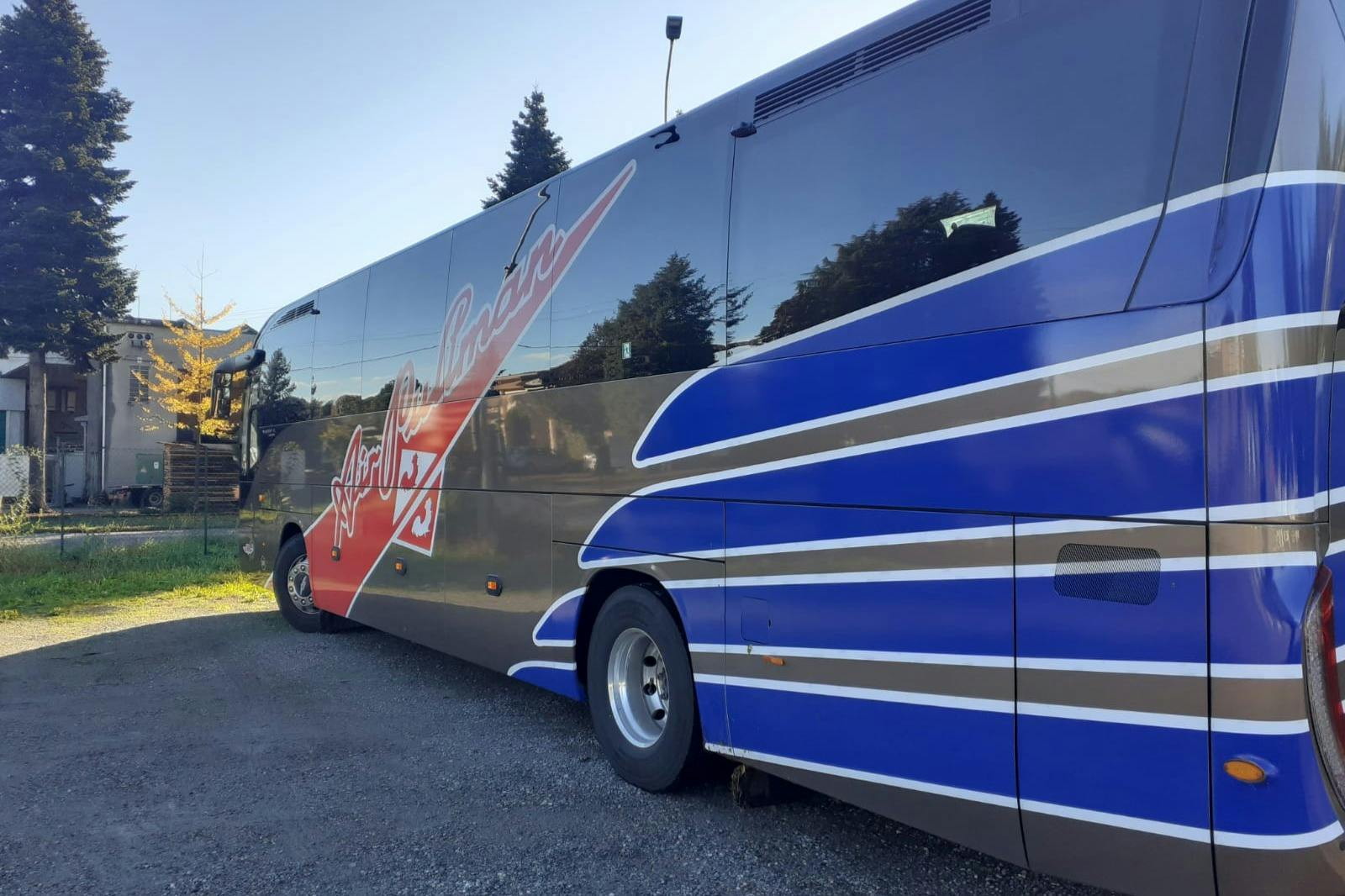 A parked bus with a blue, gray, and white design, featuring a red stripe and the word "Lovelock" on the side. Trees in the background.