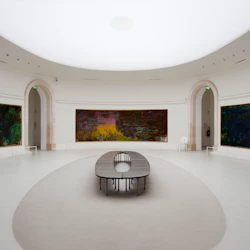 Ett rymligt, ovalt rum med stora, färgglada målningar på böjda väggar och en minimalistisk, oval bänk i mitten.