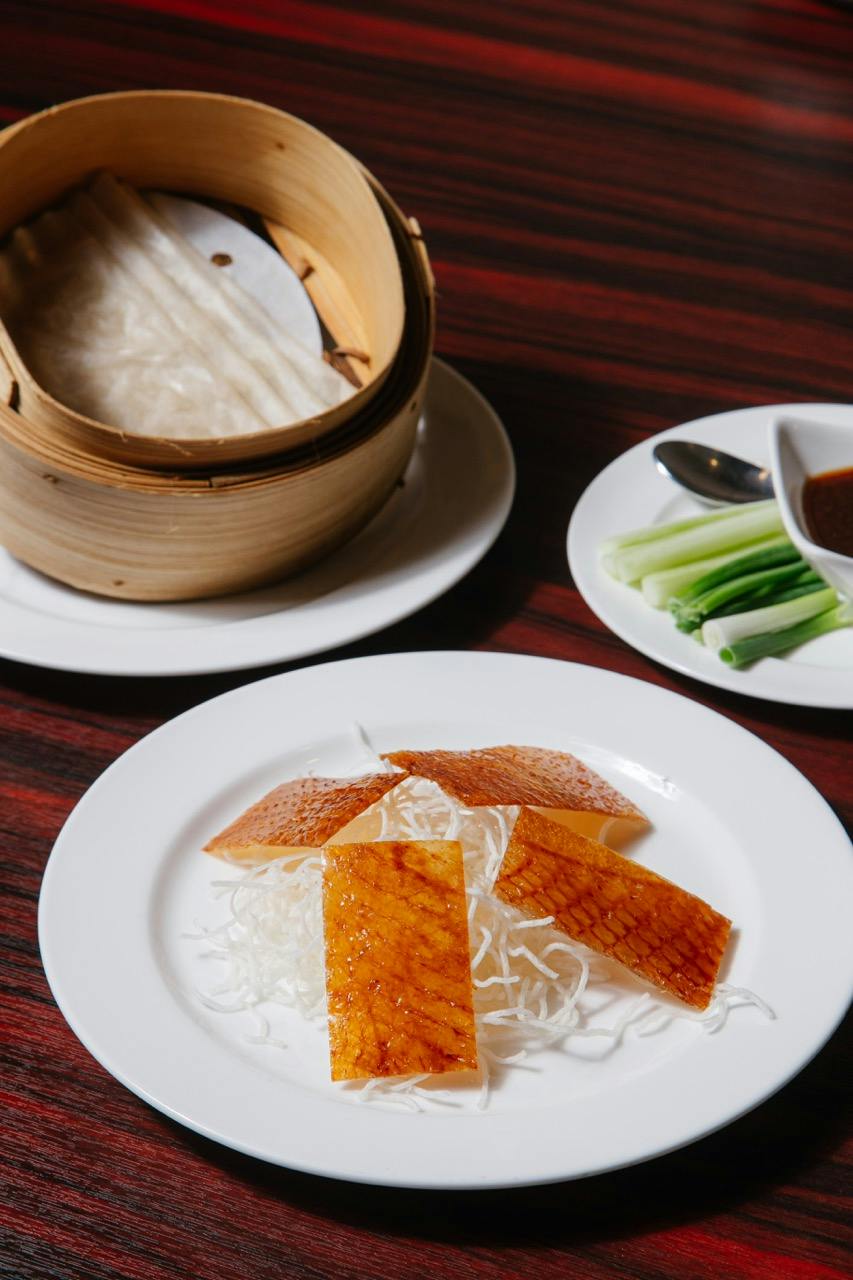 A serving of crispy duck skin on shredded vegetables, with pancakes, green onions, and sauce on a wooden table.