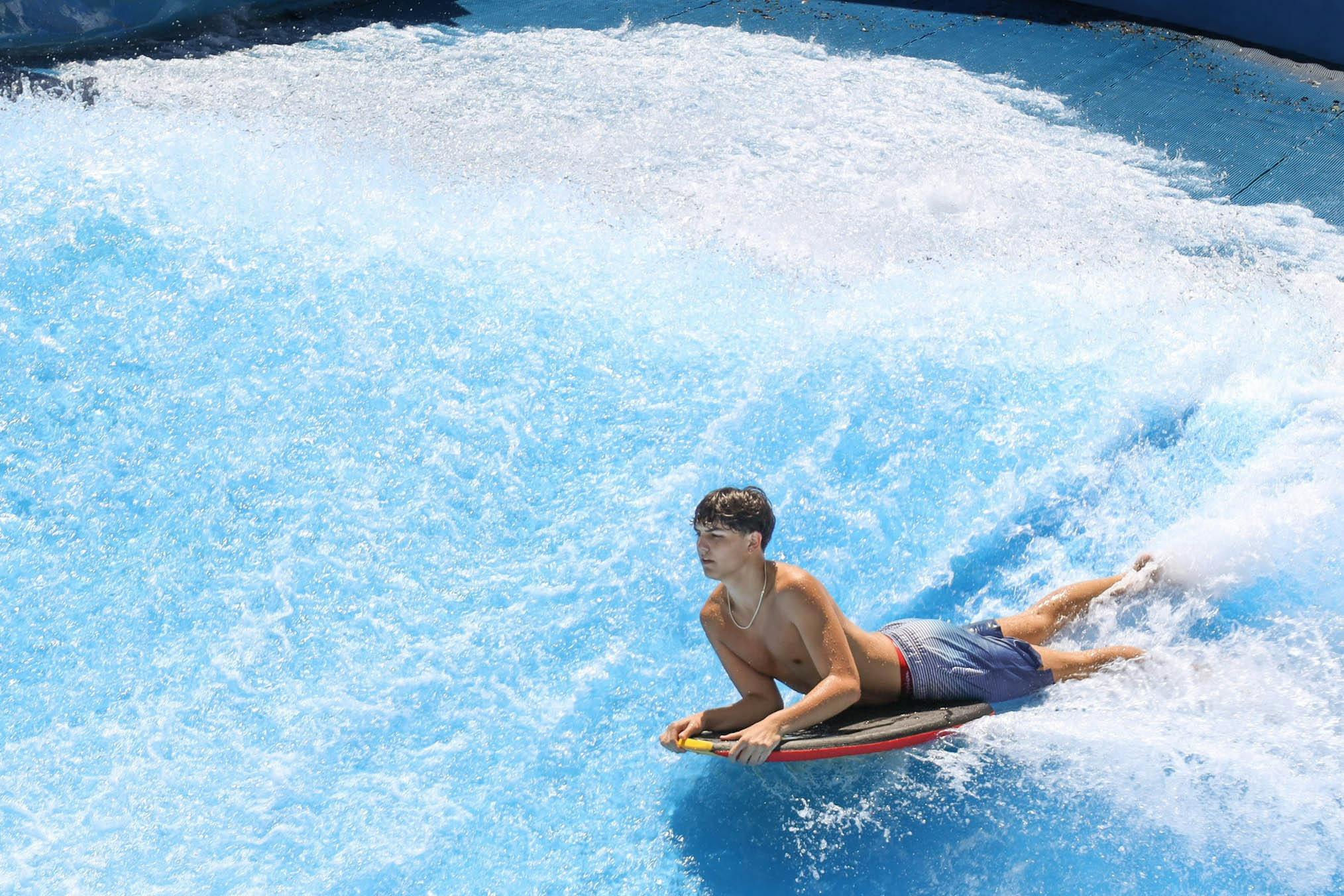 Ένα άτομο που καβαλάει ένα bodyboard σε ένα μπλε τεχνητό κύμα σε ένα υδάτινο πάρκο.