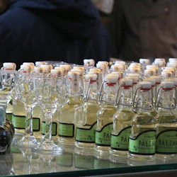 Rader av små flaskor med olika etiketter och mönster, omgivna av tomma glas, sannolikt utställda på en marknad eller butik.