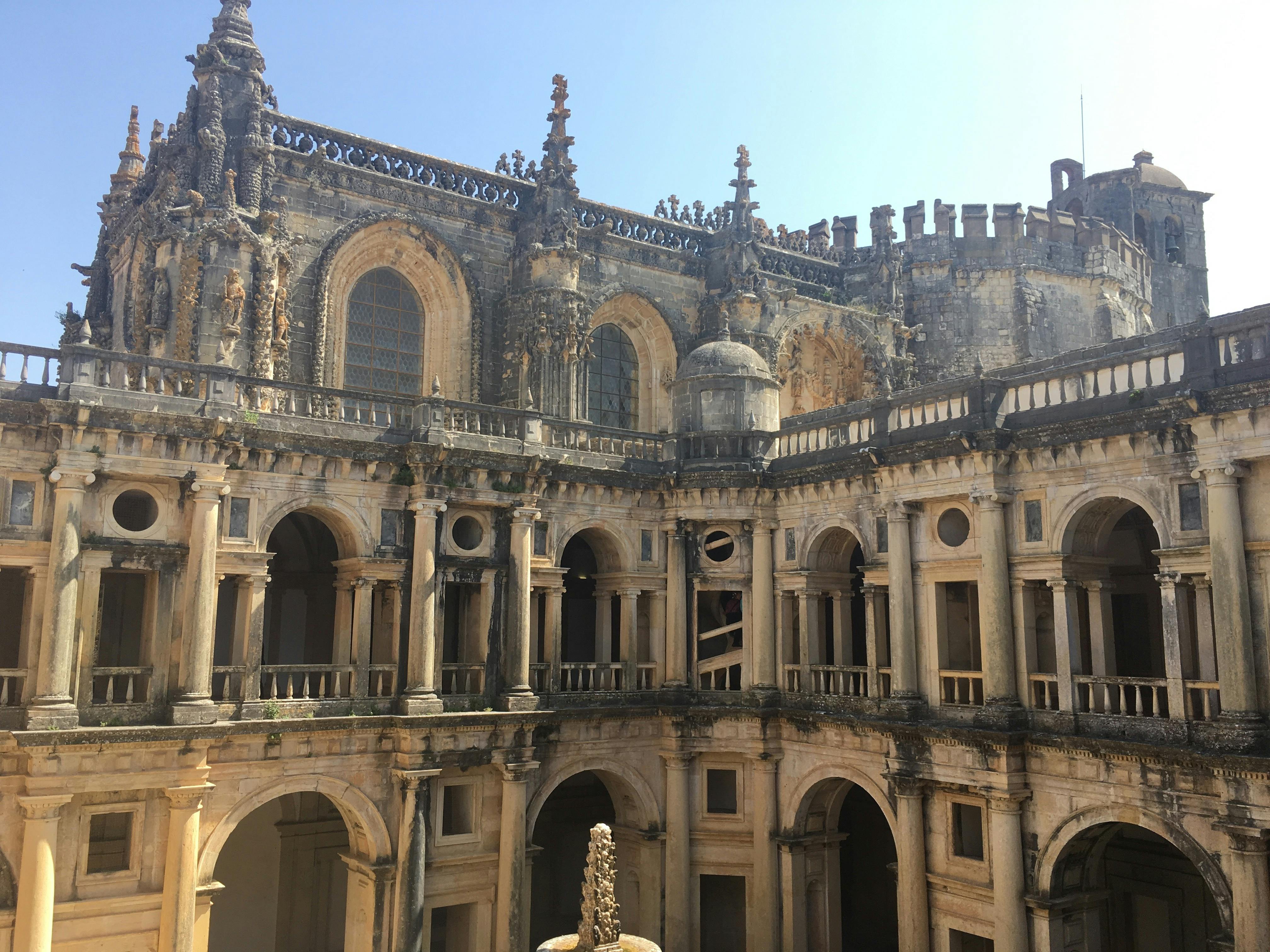 澄んだ青い空の下に、複数のアーチ、詳細な石の彫刻、大きなアーチ型の窓がある華やかな古代の建物。