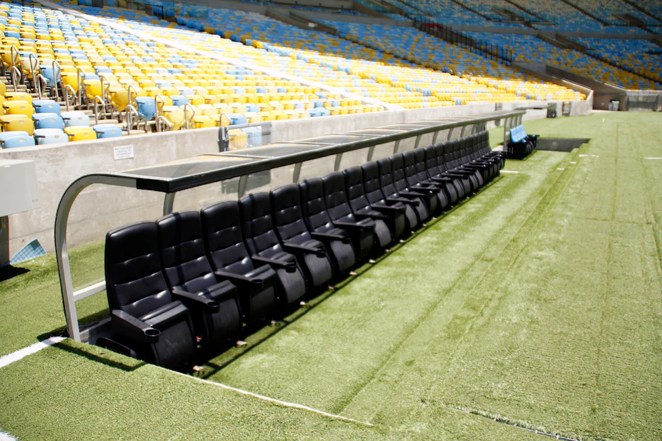 Rows of black stadium seats under a shelter, with yellow and blue seating visible in the background.