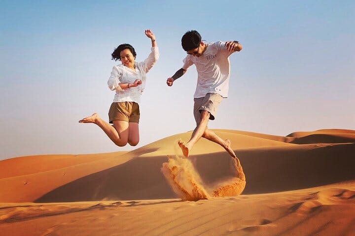 两个人愉快地跳上沙丘，背景是晴朗的蓝天。