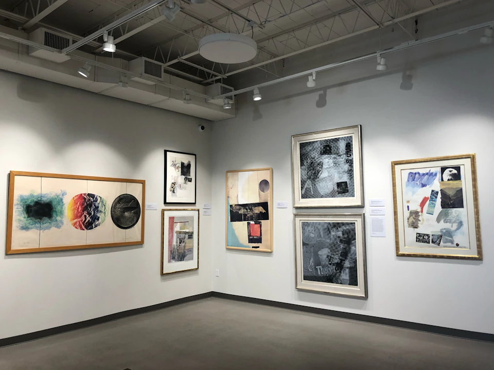 An art gallery with framed abstract paintings on white walls, under ceiling spotlights.