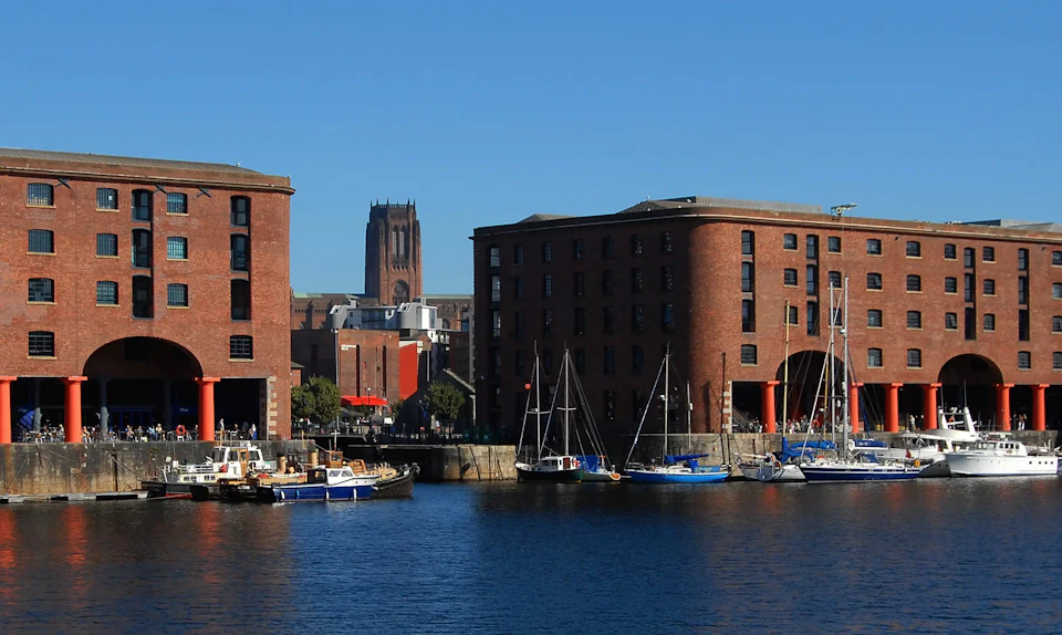 Red-brick buildings and docked sailboats by a waterfront under a clear blue sky. Tall church tower visible in the background.