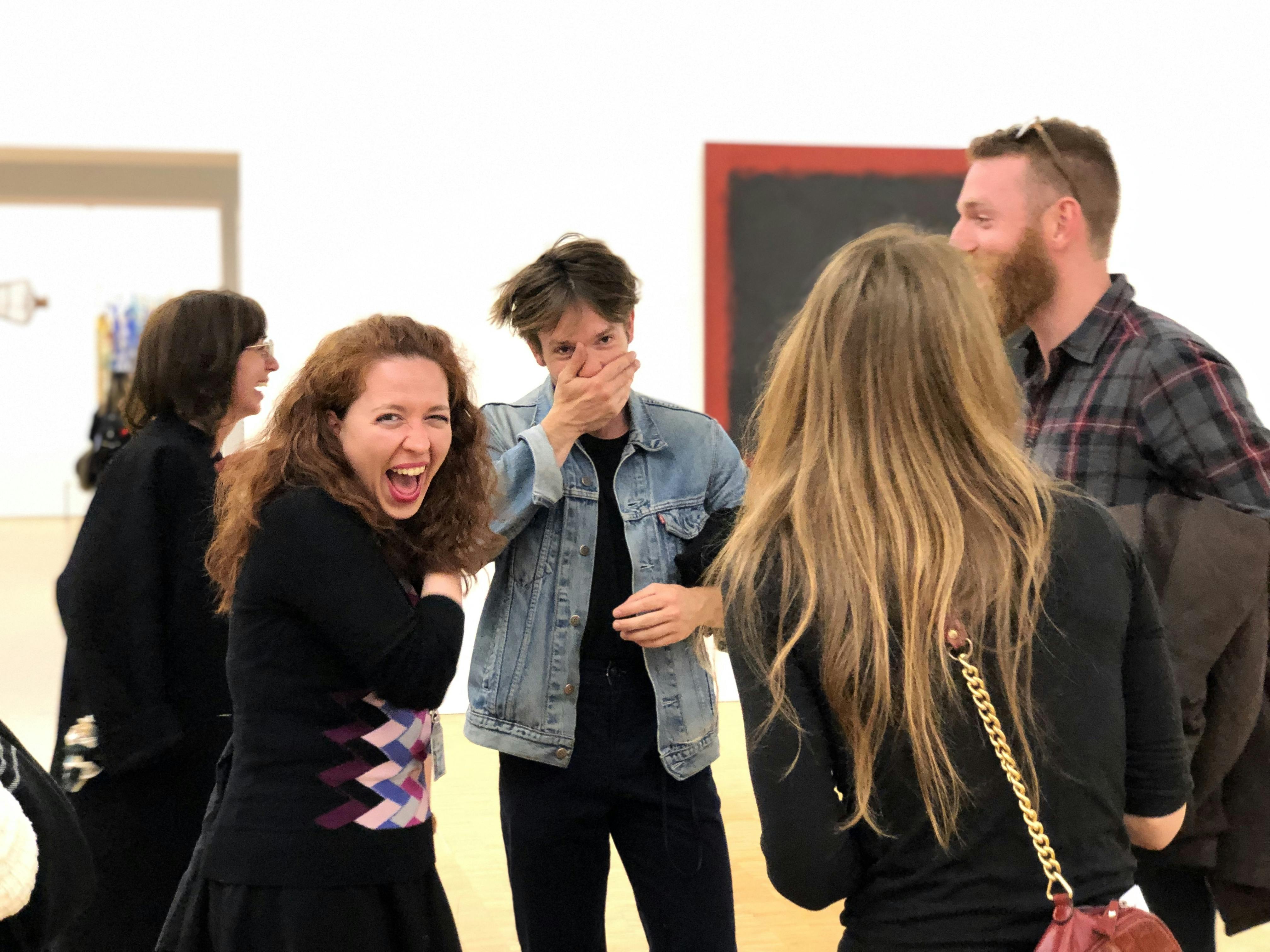 Ομάδα ανθρώπων που γελούν και συνομιλούν σε μια γκαλερί τέχνης, με ένα άτομο να καλύπτει το στόμα του.