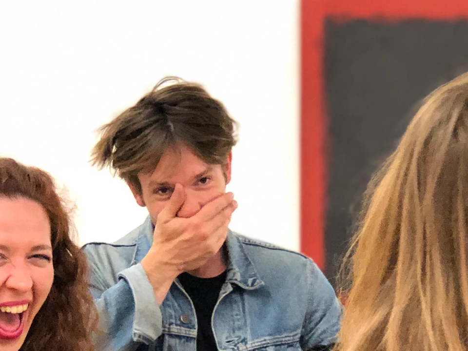 Group of people laughing and conversing in an art gallery, with one person covering their mouth.