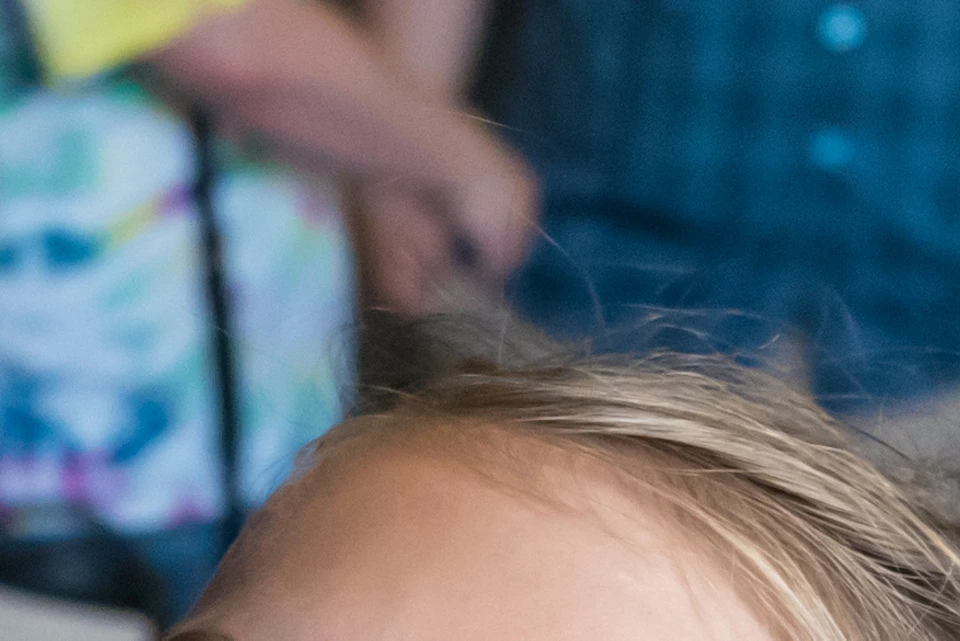 Smiling girl in a pink shirt holds a climbing rope. People, including a couple, stand in the background at an indoor activity center.