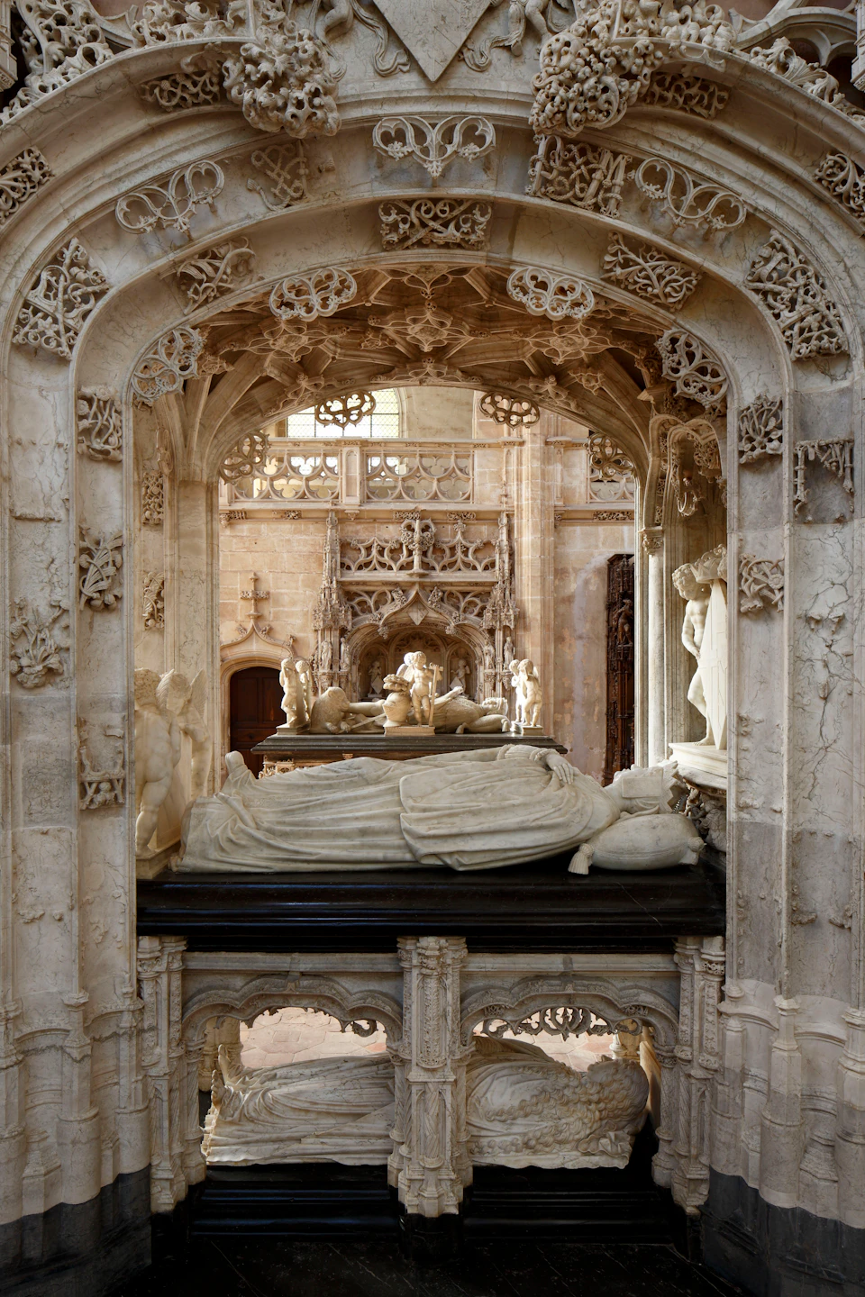 Ornate stone tombs with detailed carvings and statues inside a gothic-style cathedral.