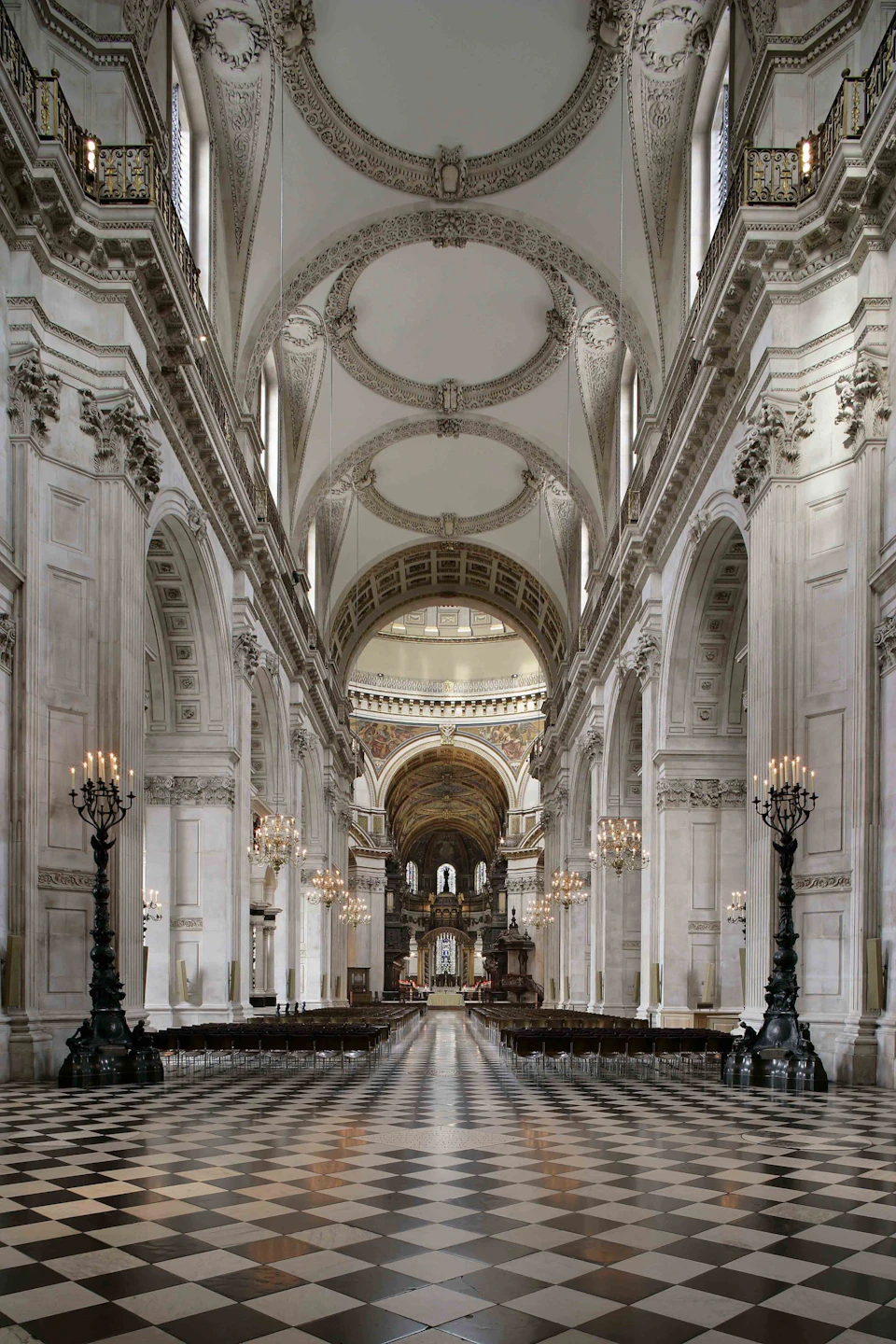 Grand cathedral interior with high vaulted ceilings, ornate arches, chandeliers, and rows of empty chairs leading to an altar.