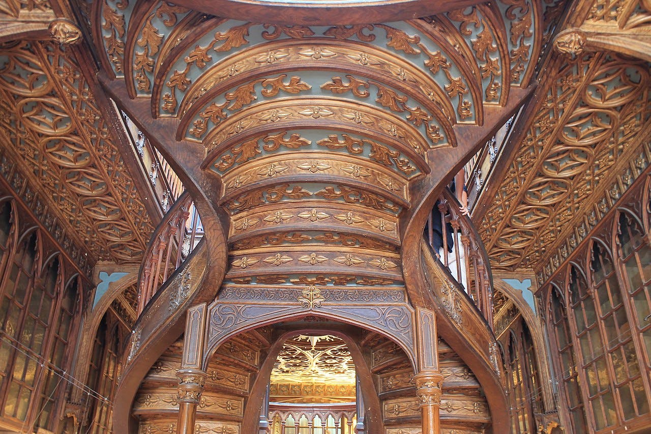 Zdobené dřevěné točité schodiště se složitými řezbami a dekorativními oblouky v propracovaně řešeném interiéru budovy.