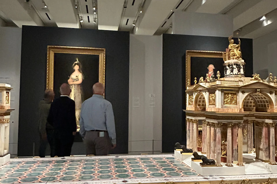 Visitors observing a framed portrait of a woman in a museum gallery with patterned floor tiles and modern lighting.