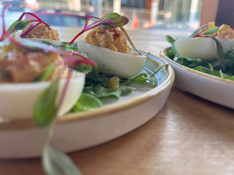 Close-up of deviled eggs garnished with herbs and microgreens on a white plate, placed on a wooden surface.