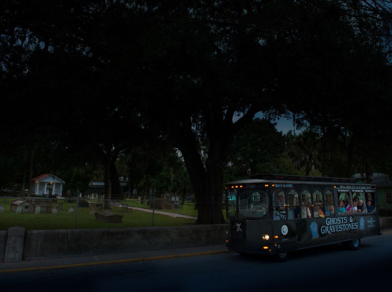 A bus labeled "Ghost and Graves" drives past a dimly-lit cemetery with large trees and gravestones.