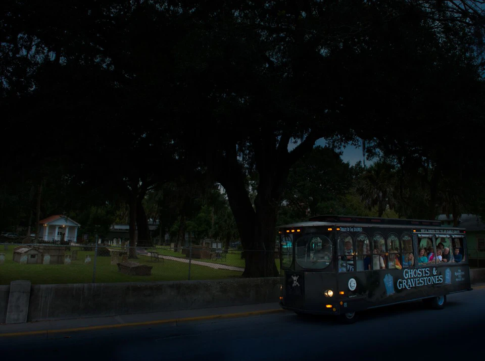 A bus labeled "Ghost and Graves" drives past a dimly-lit cemetery with large trees and gravestones.