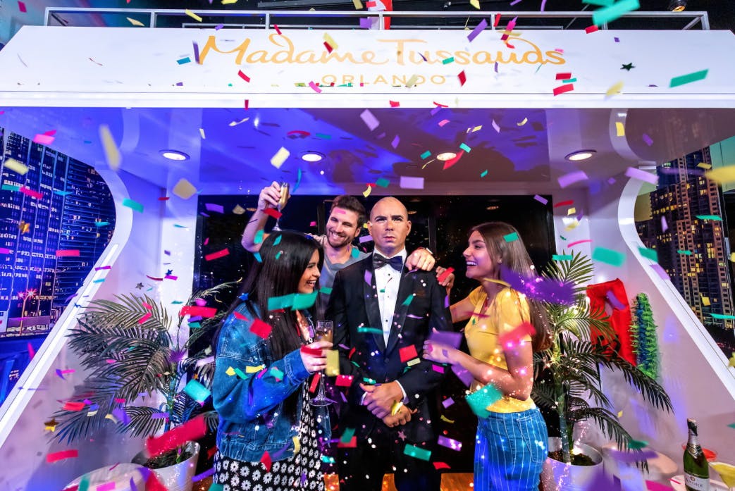 三个人在奥兰多杜莎夫人蜡像馆（ Madame Tussauds Orlando ）的燕尾服中围着蜡像庆祝。