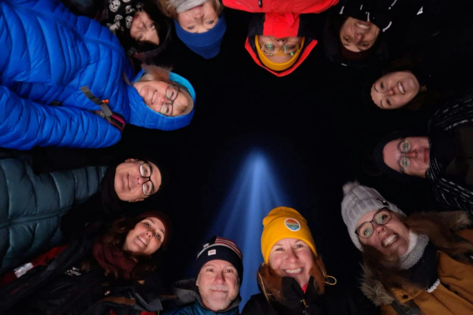 一群人站在一个圆圈里，对着镜头微笑。 背景是Imagine Peace Tower的灯光。