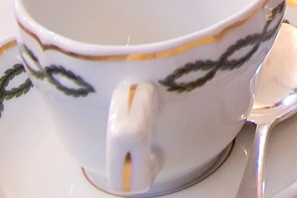 Elegant tea setup featuring a three-tier stand with sandwiches, pastries, and desserts; teacup and saucer on the table in a cozy room.
