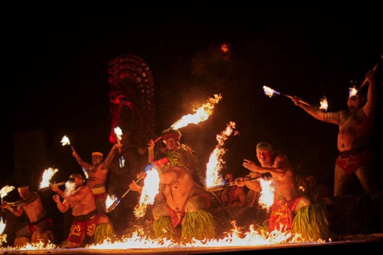 Performers in traditional attire manipulate flaming torches during a fire dance performance at night.