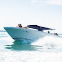 A speedboat with a blue canopy moving quickly over water, with several people onboard enjoying the ride.