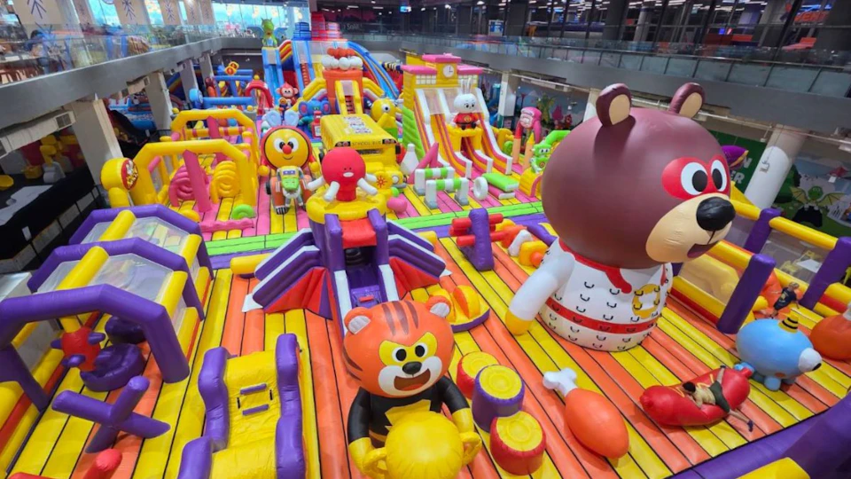 Colorful indoor inflatable playground with slides and cartoon-themed structures in a shopping mall setting.