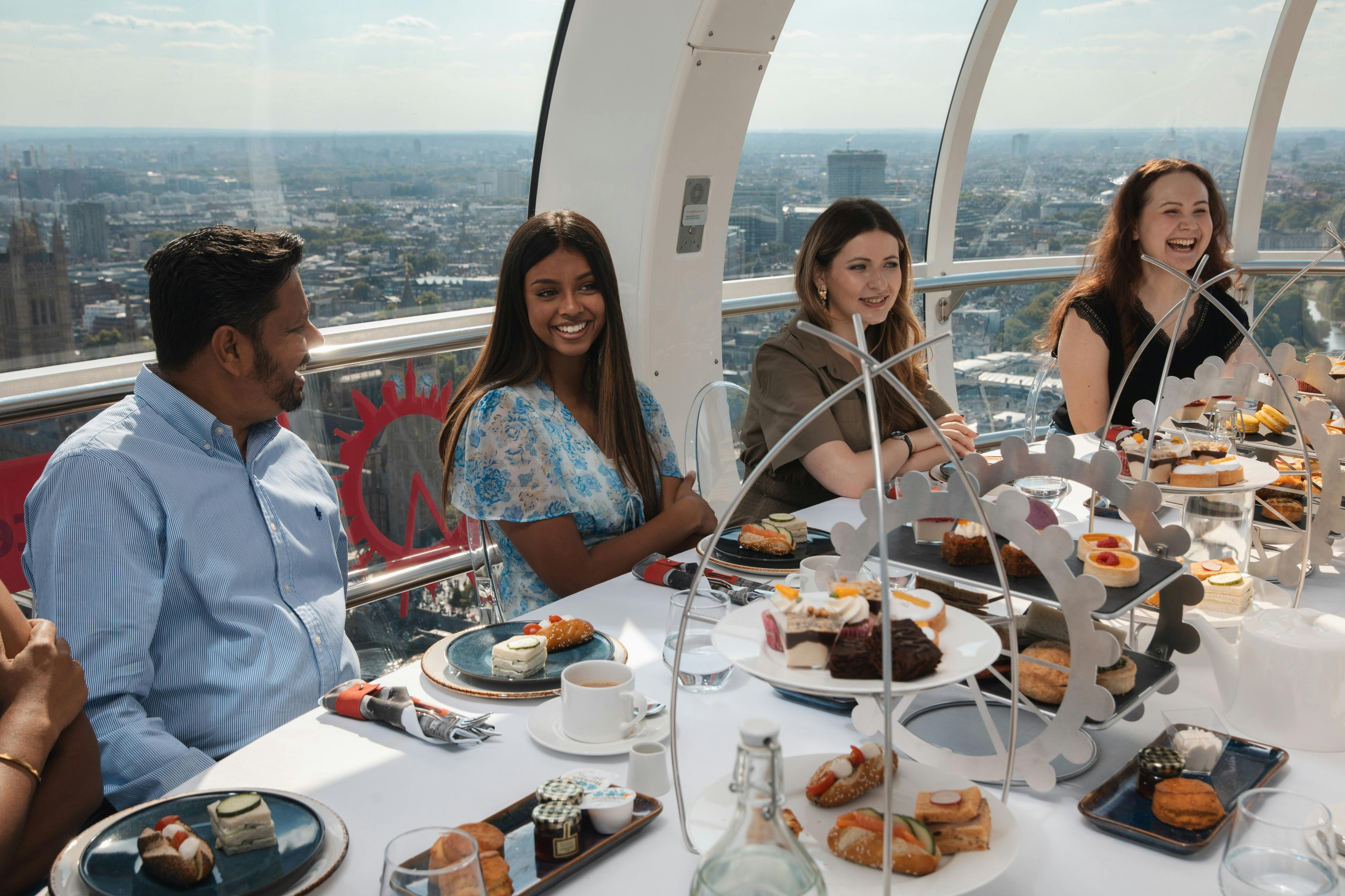 Three people seated at a table in a glass-enclosed space with city views, enjoying a spread of pastries and tea.