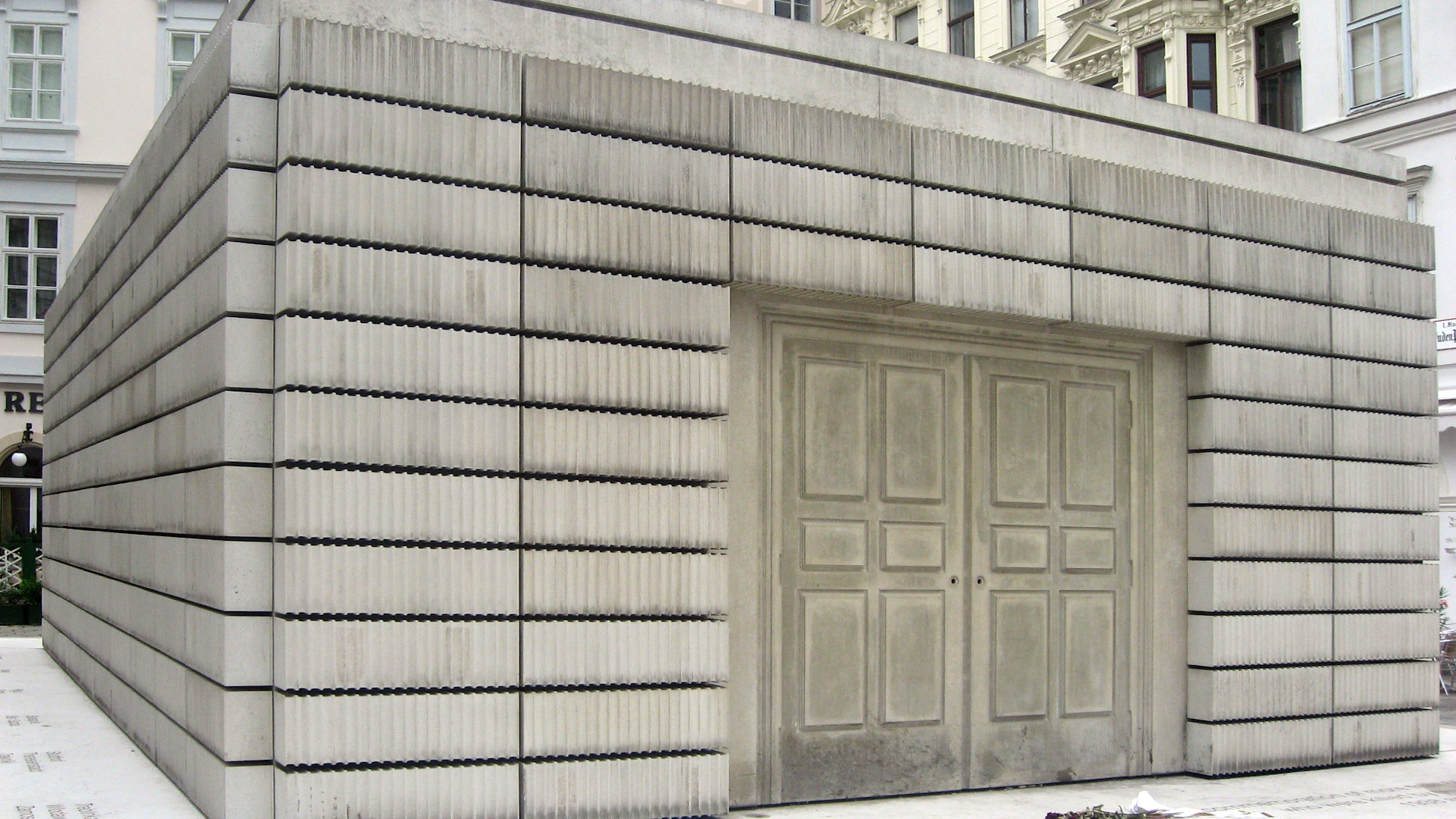 A concrete building facade with a large double door and ribbed, horizontal paneling.