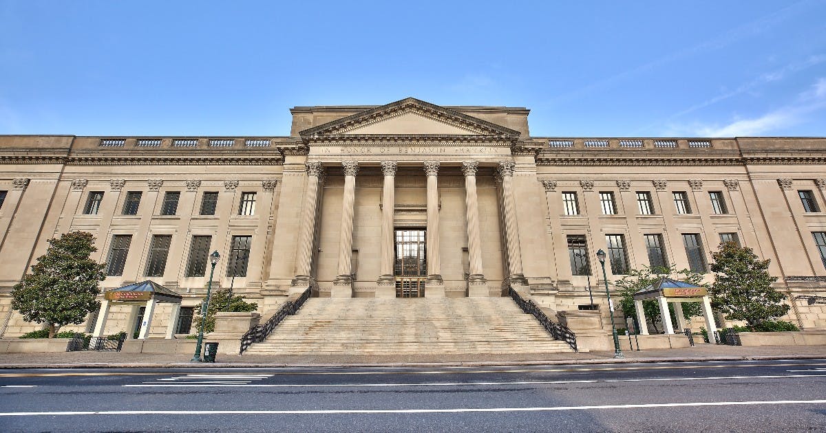 澄んだ青空の下、6本の柱、広い階段、三角形のペディメントを備えた新古典主義の建物。