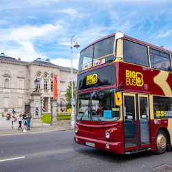 En dubbeldäckad turnébuss märkt "Big Bus Dublin" kör förbi en historisk stenbyggnad med människor som står i närheten.