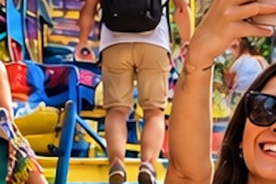 A couple takes a selfie on colorful stairs with people seated at tables and vibrant decor in the background.