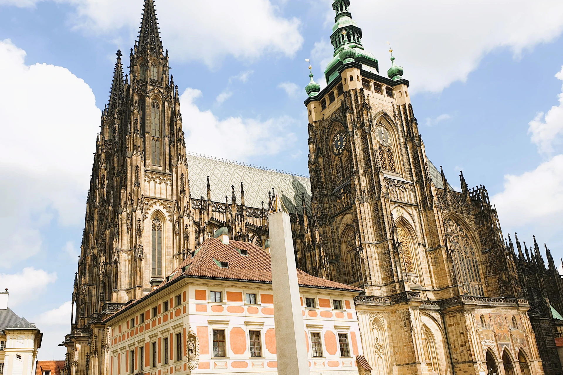 A historic cathedral with ornate towers and a smaller colorful building in front, under a partly cloudy sky.