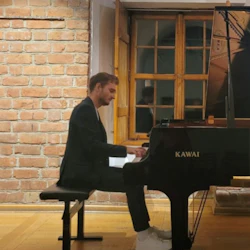 En person som spelar flygel i ett rum med tegelvägg och träfönster.