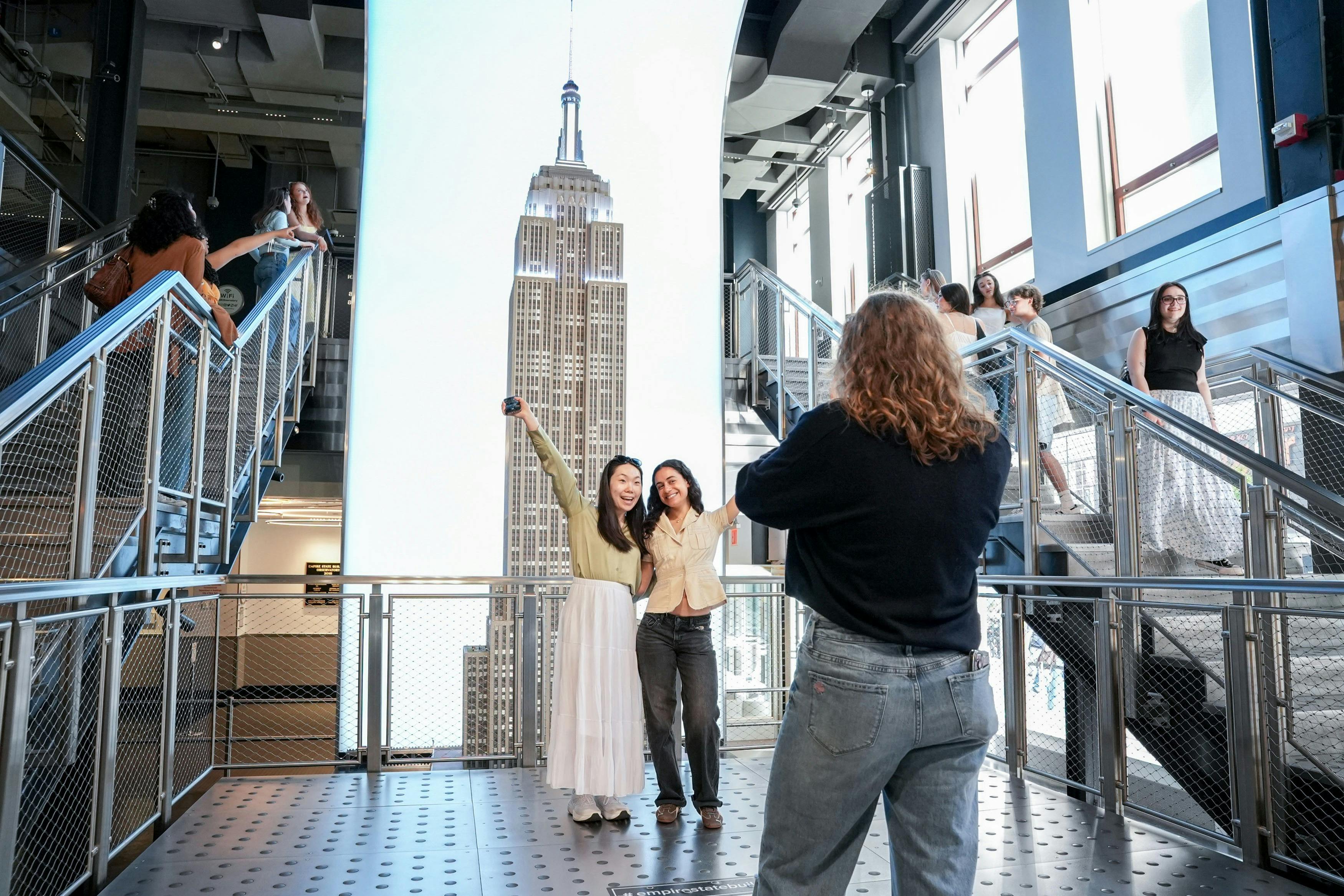 Due donne posano per una foto davanti a uno schermo su cui si vede l'Empire State Building, mentre un'altra persona le scatta la foto.