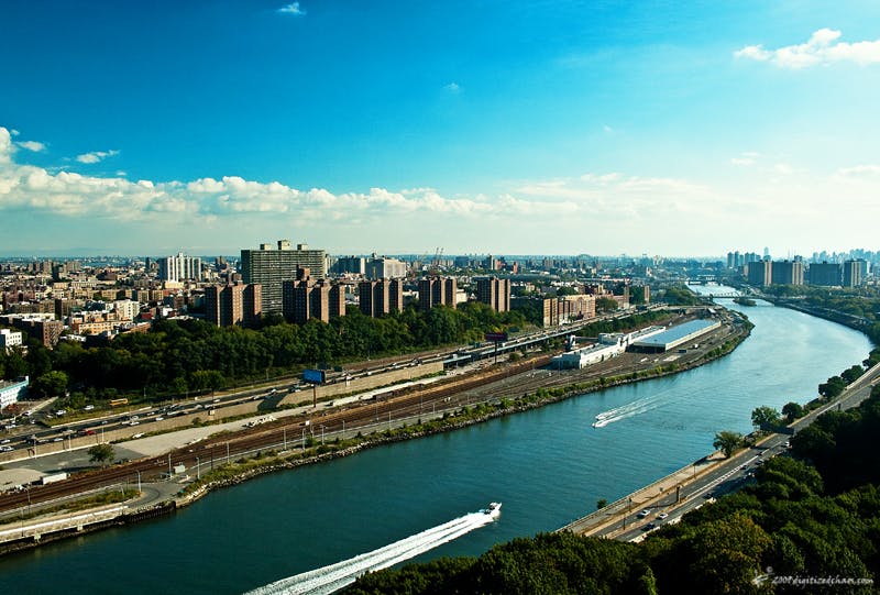 鸟瞰城市，河流、高层建筑、绿色空间和船只在蓝天下的水上小径。