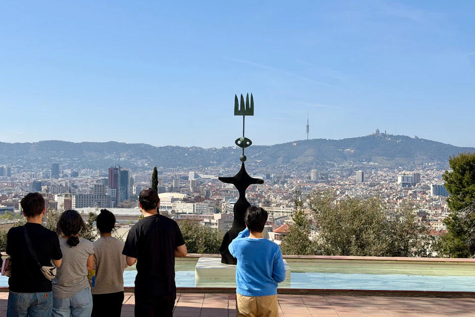 Four people stand near a statue with a cityscape and distant hills in the background on a sunny day.