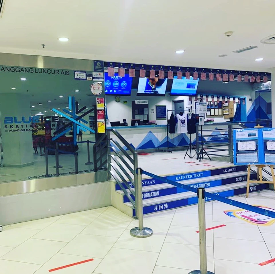 Ticket counter area for an ice skating rink, with glass walls, blue-themed decorations, and signs in multiple languages.