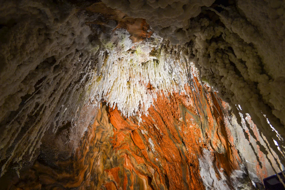 A cave ceiling with intricate white stalactites and vibrant orange and brown mineral formations.