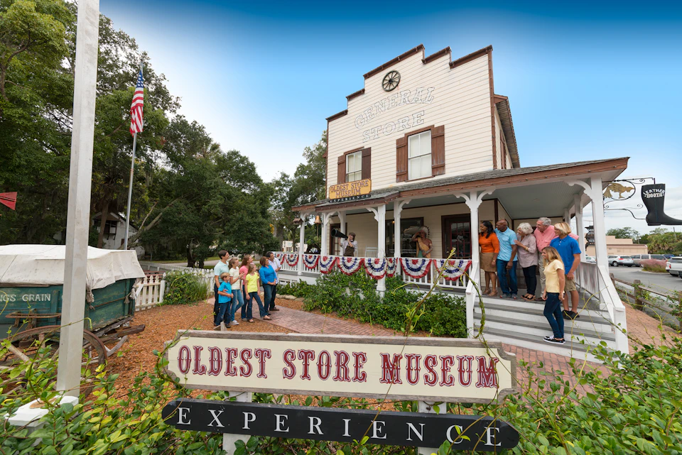 People gather outside the Oldest Store Museum, decorated with patriotic bunting, next to a sign reading "Oldest Store Museum Experience."