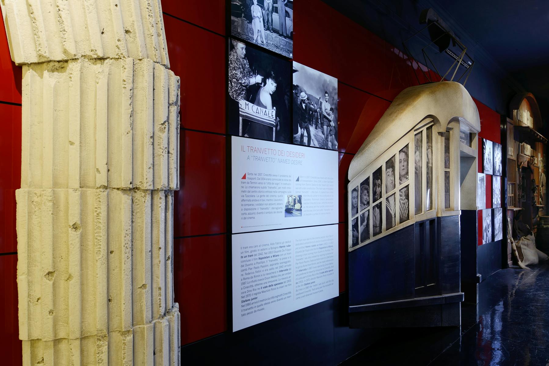 Un allestimento in un museo che mostra fotografie d'epoca e didascalie su una parete rossa e nera, con un tram in esposizione sul lato.