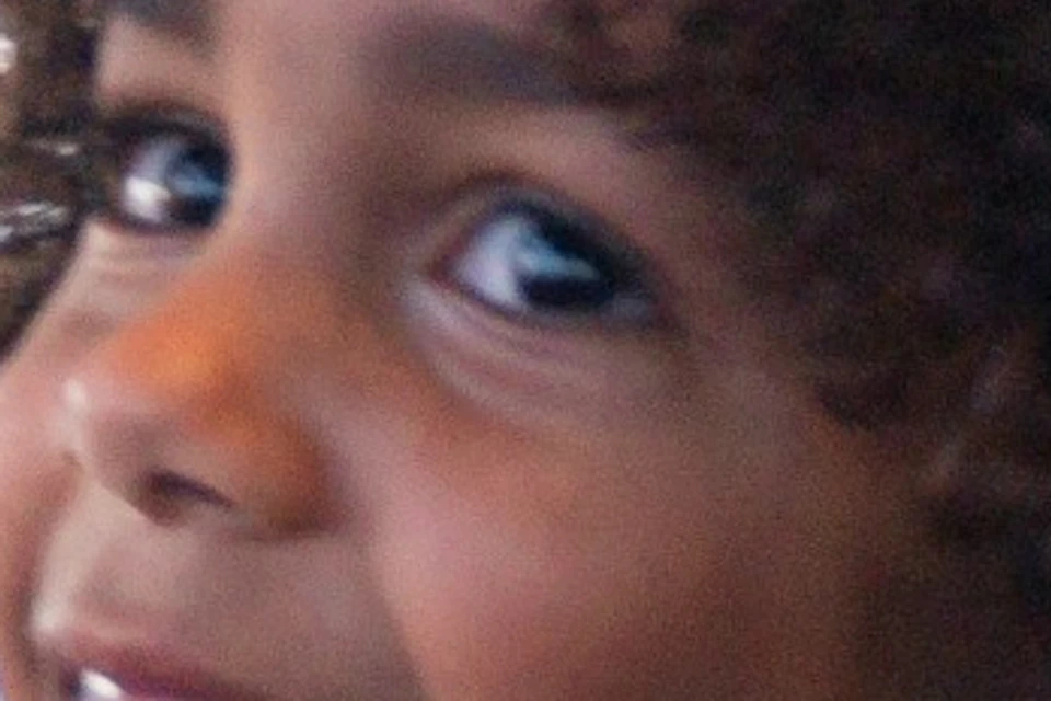 A child with curly hair, wearing a black shirt, smiles while interacting with a white robot in a room with large windows.