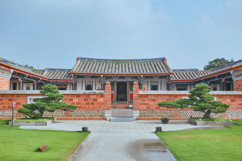 Traditional East Asian building with a tiled roof, red brick walls, and a paved path leading through a landscaped garden.