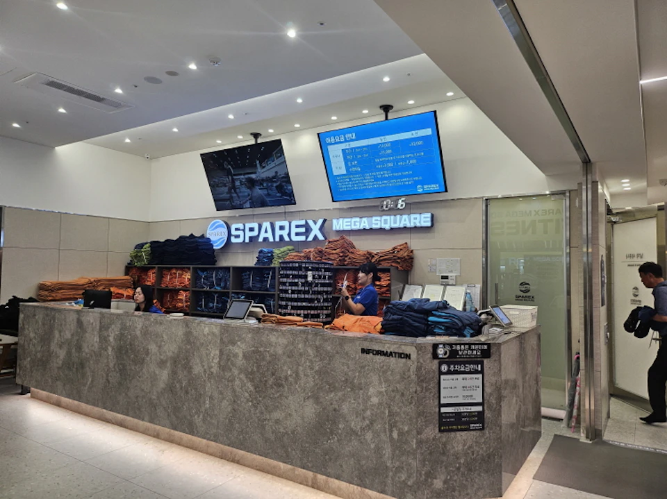 Reception area of a spa facility with staff, folded towels, a counter, and information displayed on screens.