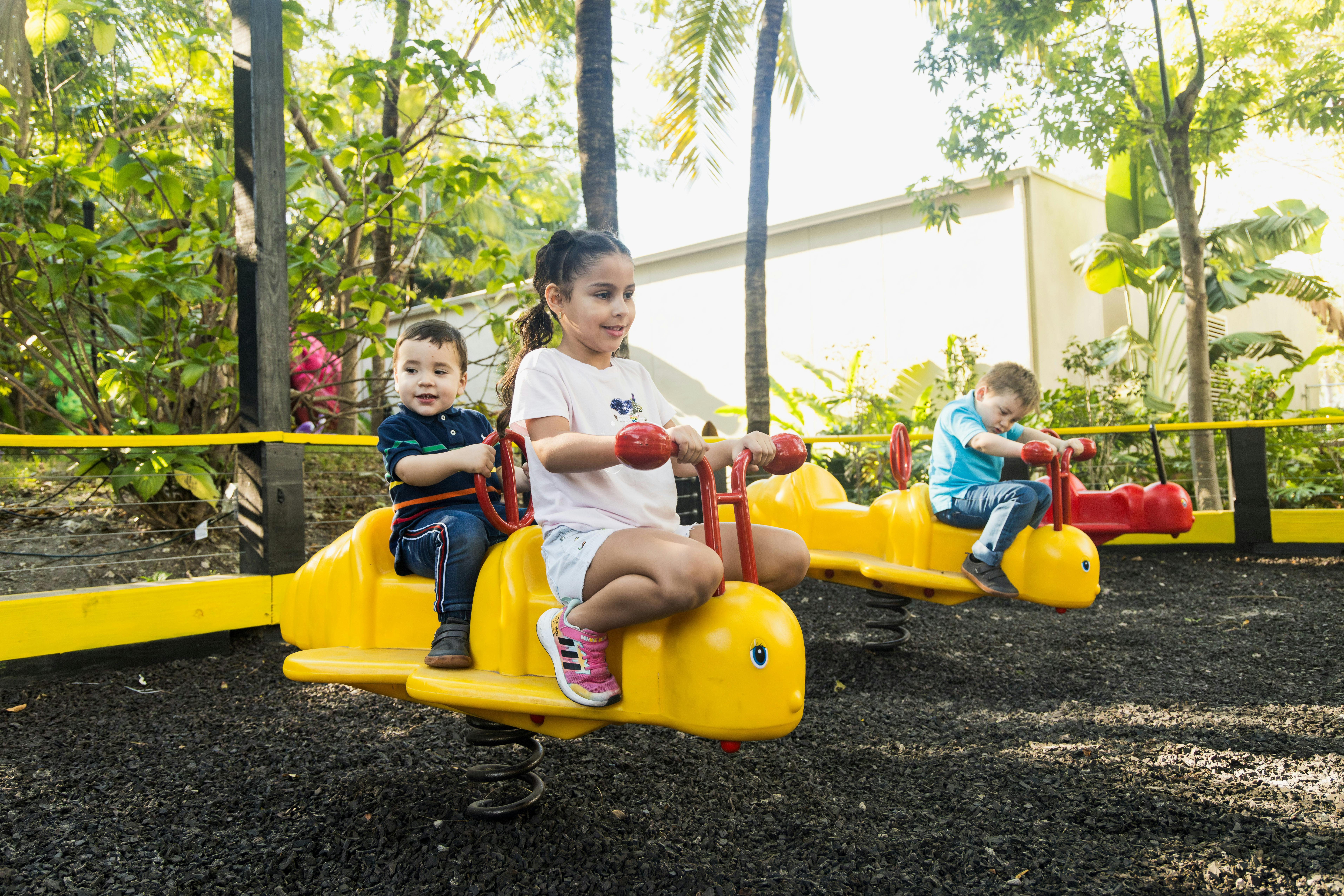 木や緑を背景にした公園で、黄色い動物の形をしたシーソーで遊ぶ子供たち。
