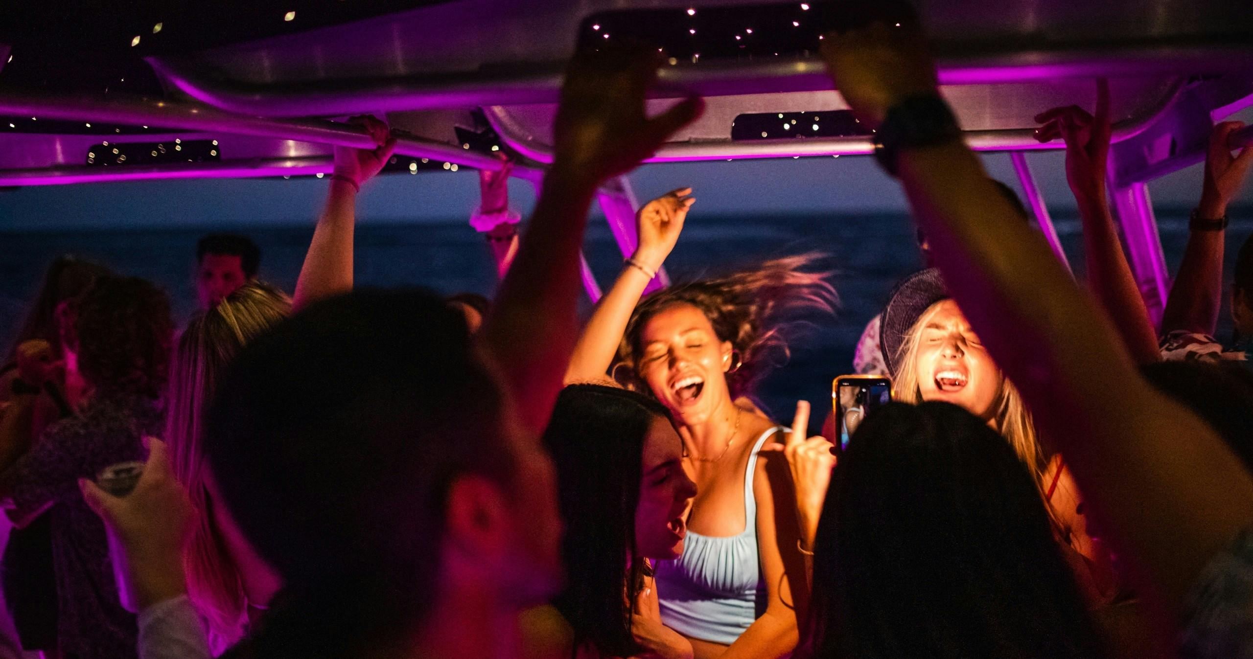 Un grupo de personas bailando y disfrutando de una fiesta en un barco por la noche, iluminado por luces de colores.