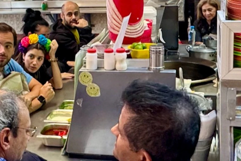 People gathered around a small food stall with colorful plates and a vase of flowers, engaging in conversation.