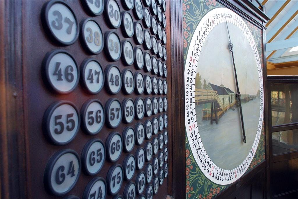 Een close-up van een vintage bingo- of loterijmachine met genummerde knoppen en een draaiende wijzer op een geïllustreerde achtergrond.