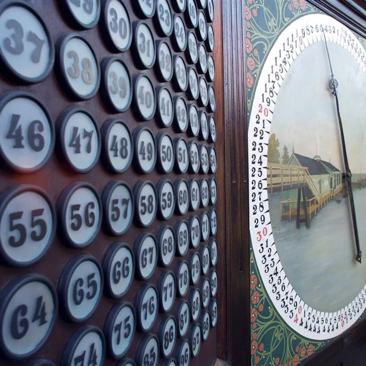 A close-up of a vintage bingo or lottery machine with numbered buttons and a rotating pointer over an illustrated backdrop.