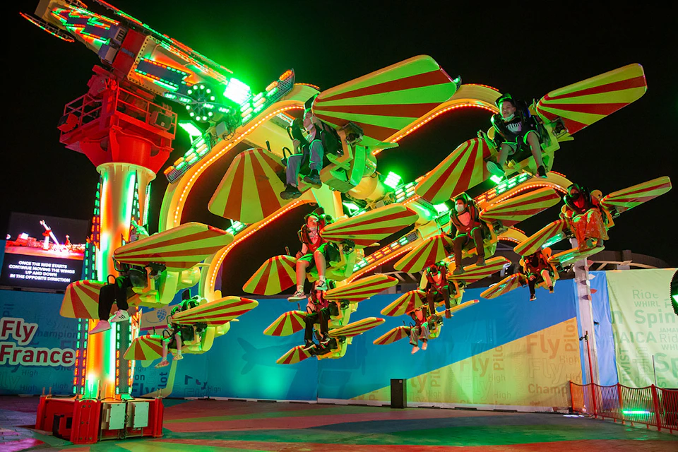 People riding a brightly lit amusement park ride with red and yellow canopies at night.