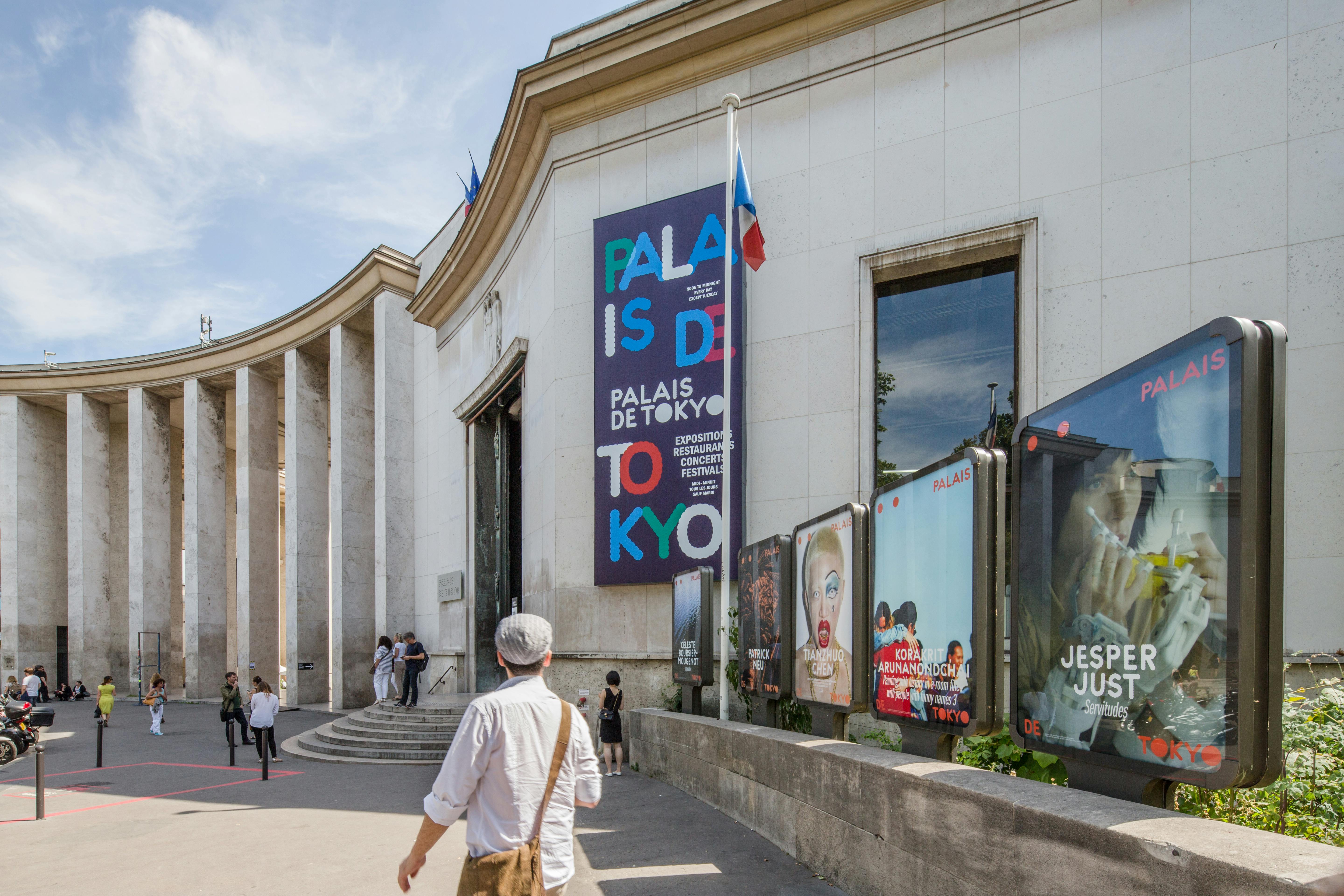 En modern byggnad med skylten "Palais de Tokyo" och annonser utanför, människor som går nära den, under en solig himmel.